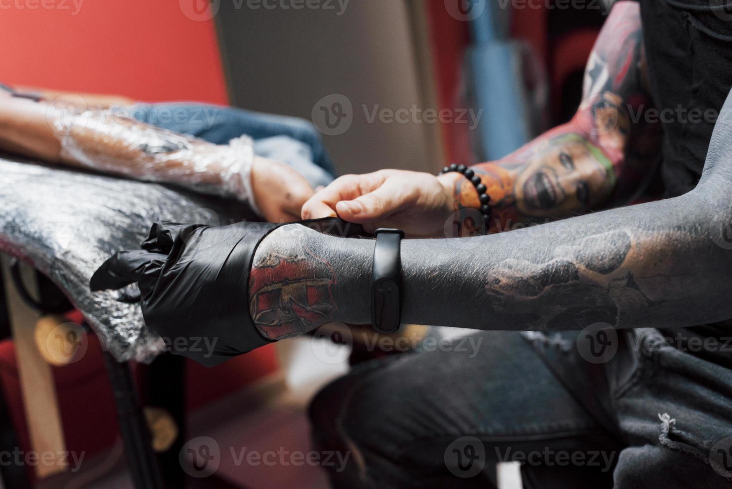 cerrar la máquina de tatuaje. Maestro en guantes negros estériles creando una imagen a mano con ella en el salón foto