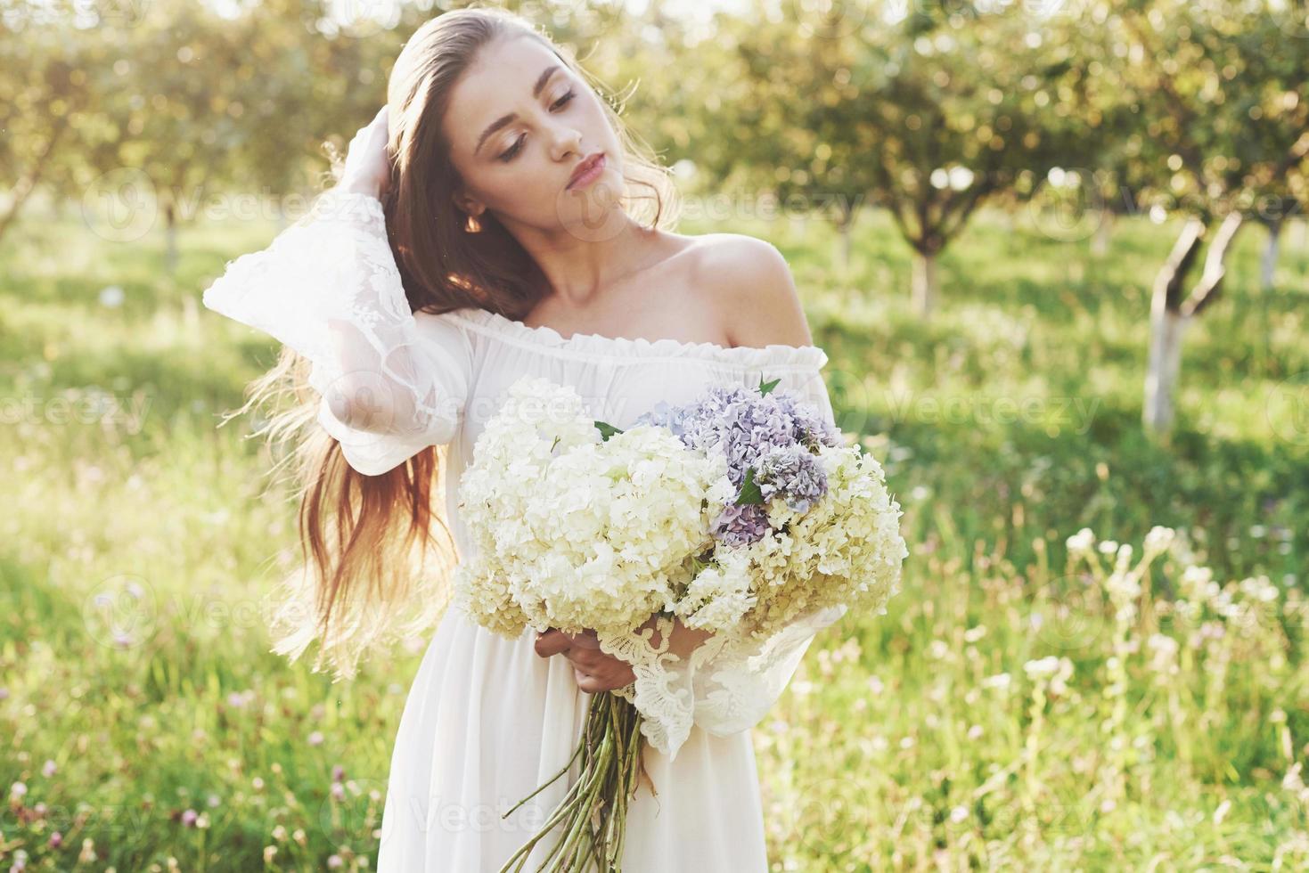 Beautiful young woman wearing elegant white dress and enjoying beautiful sunny afternoon in a summer garden photo