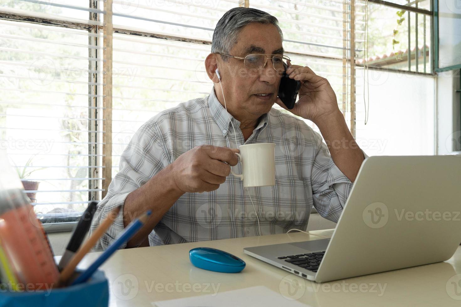 un anciano bebe una taza de café sentado frente a una computadora portátil. foto