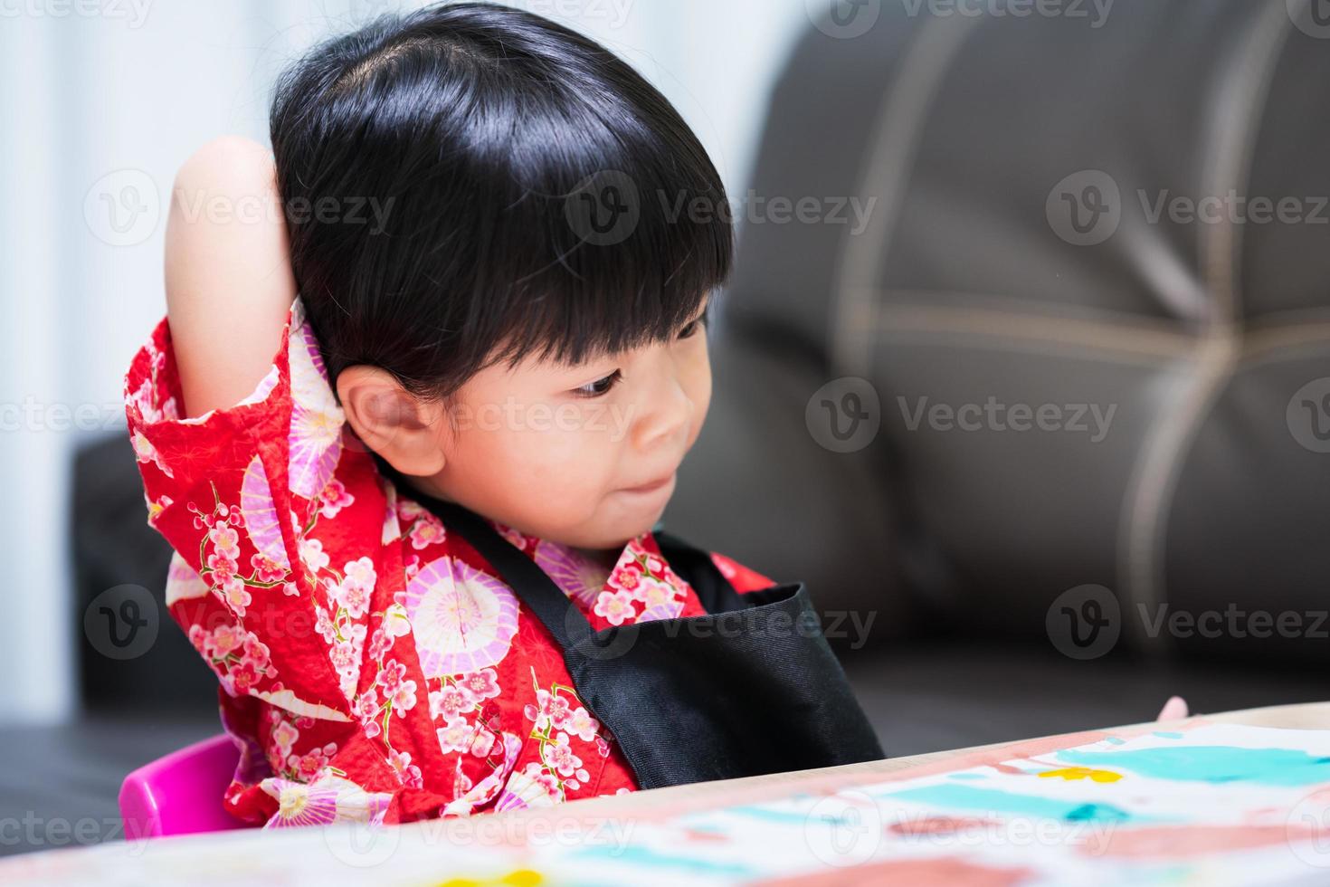 linda niña se está agarrando la espalda rascándose la espalda debido a la picazón de una etiqueta pegada a su ropa. niña vestida con una camisa roja y un delantal negro. foto