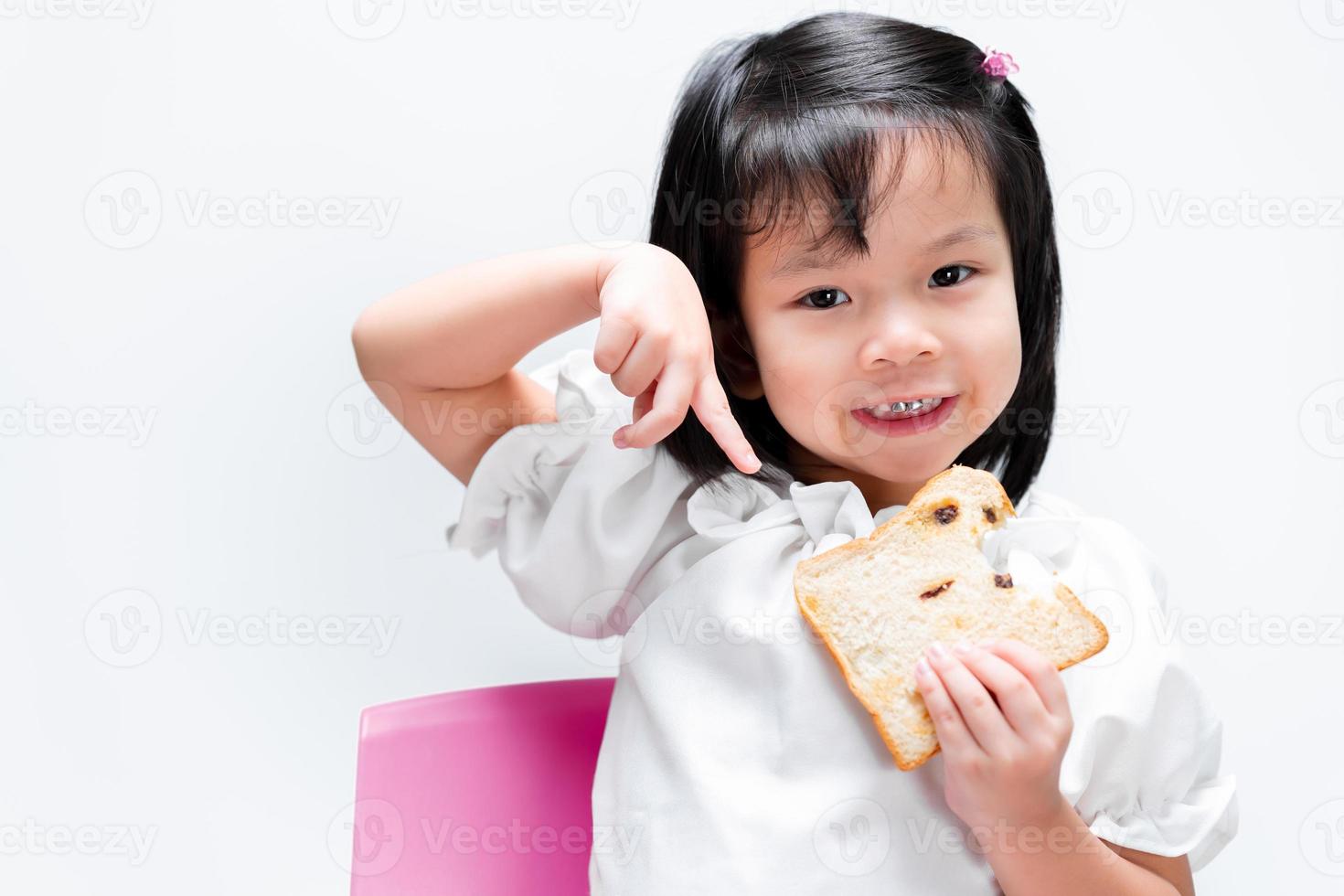 hermosa niña está feliz de comer pan. niño señala con el dedo el pan. los niños sonríen dulcemente. disfruta comiendo con el desayuno. foto