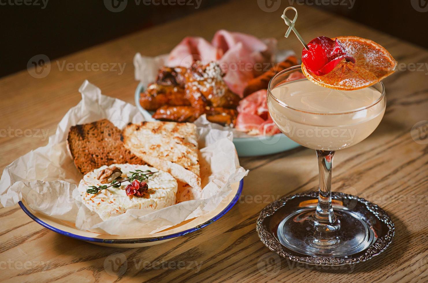 appetizing meat plate with sausage, ham, jamon, baked camembert cheese and alcohol cocktail decor photo