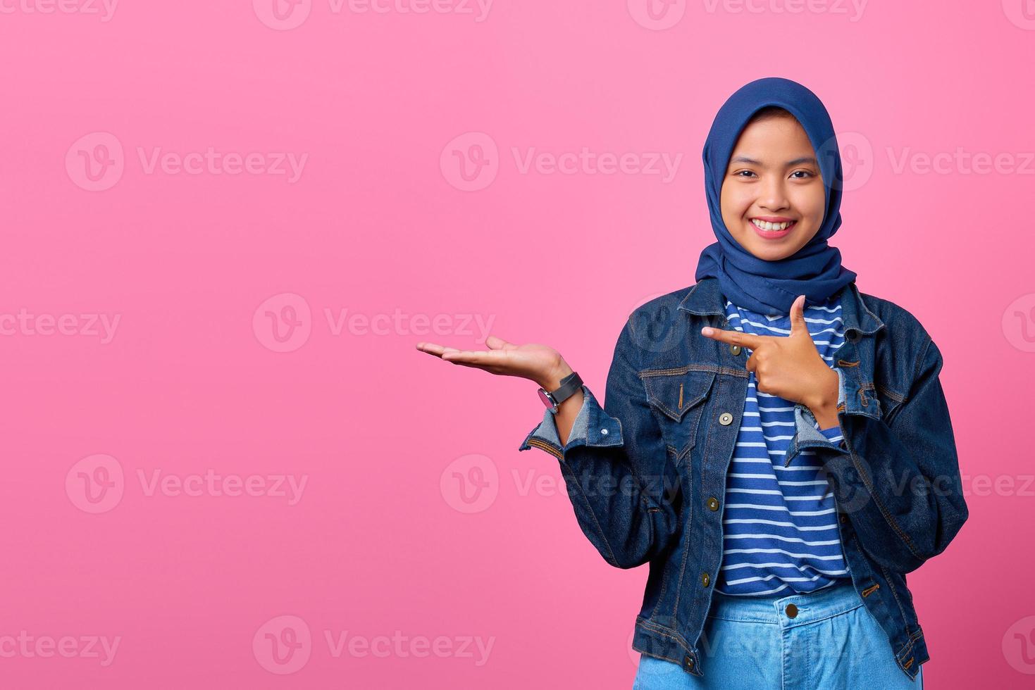 Retrato de mujer asiática joven sonriente mientras presenta el producto y apunta con el dedo foto