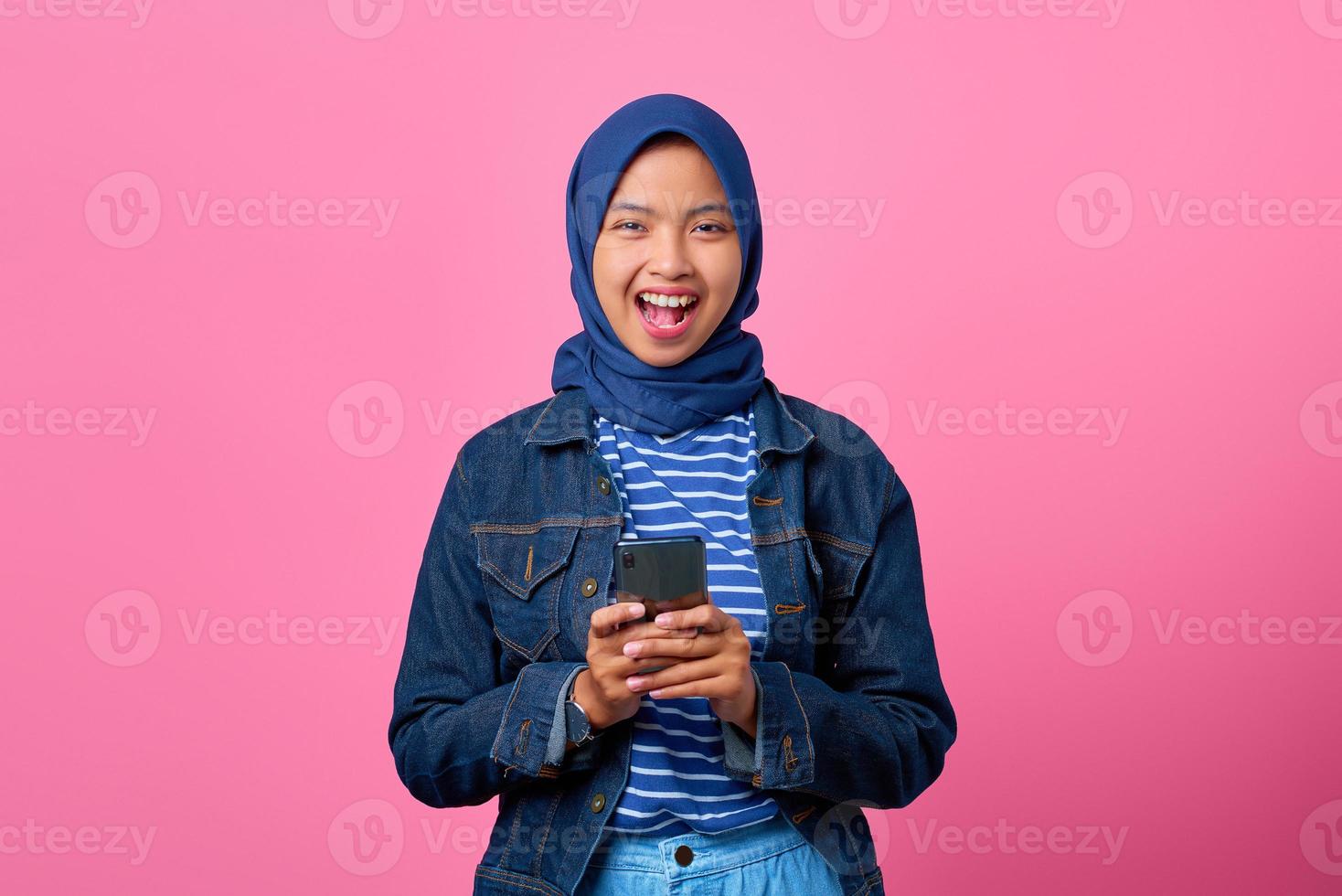 Portrait of cheerful young Asian woman holding smartphone while looking at camera photo