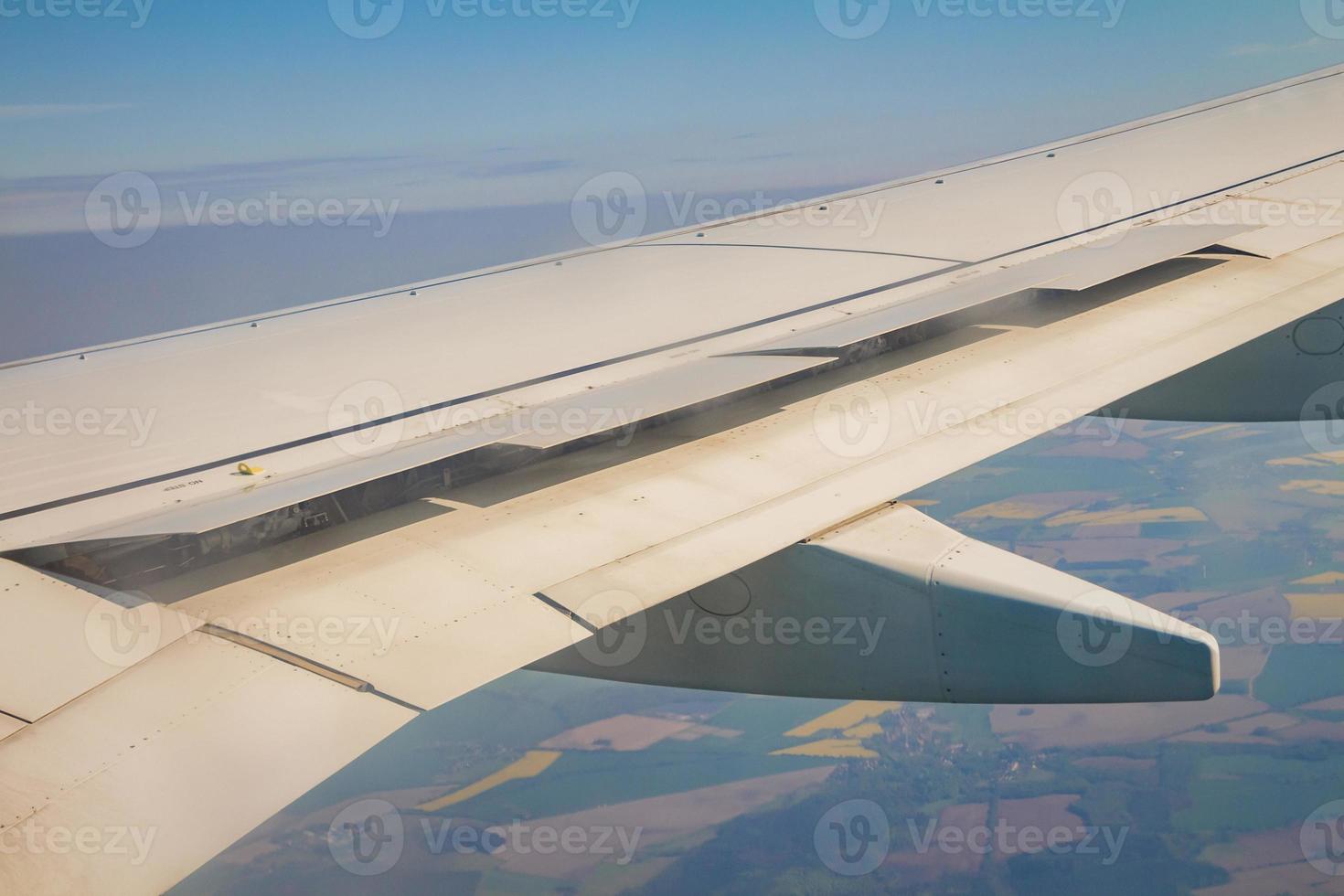 Airplane wing with the spoiler open on the sky over land photo