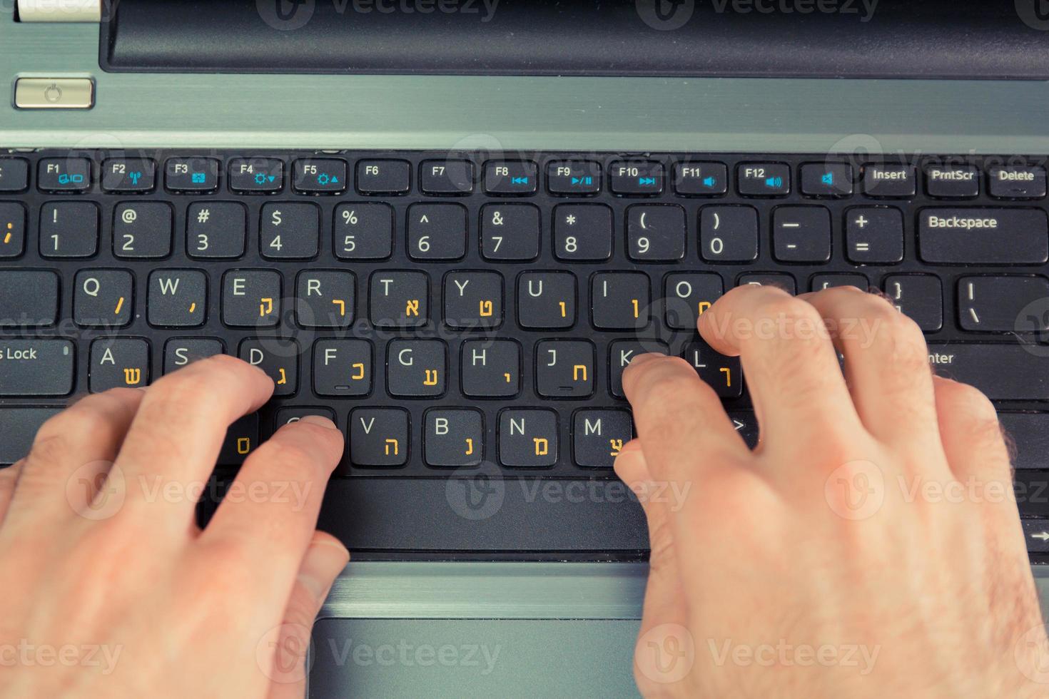 Man typing on a keyboard with letters in Hebrew and English photo
