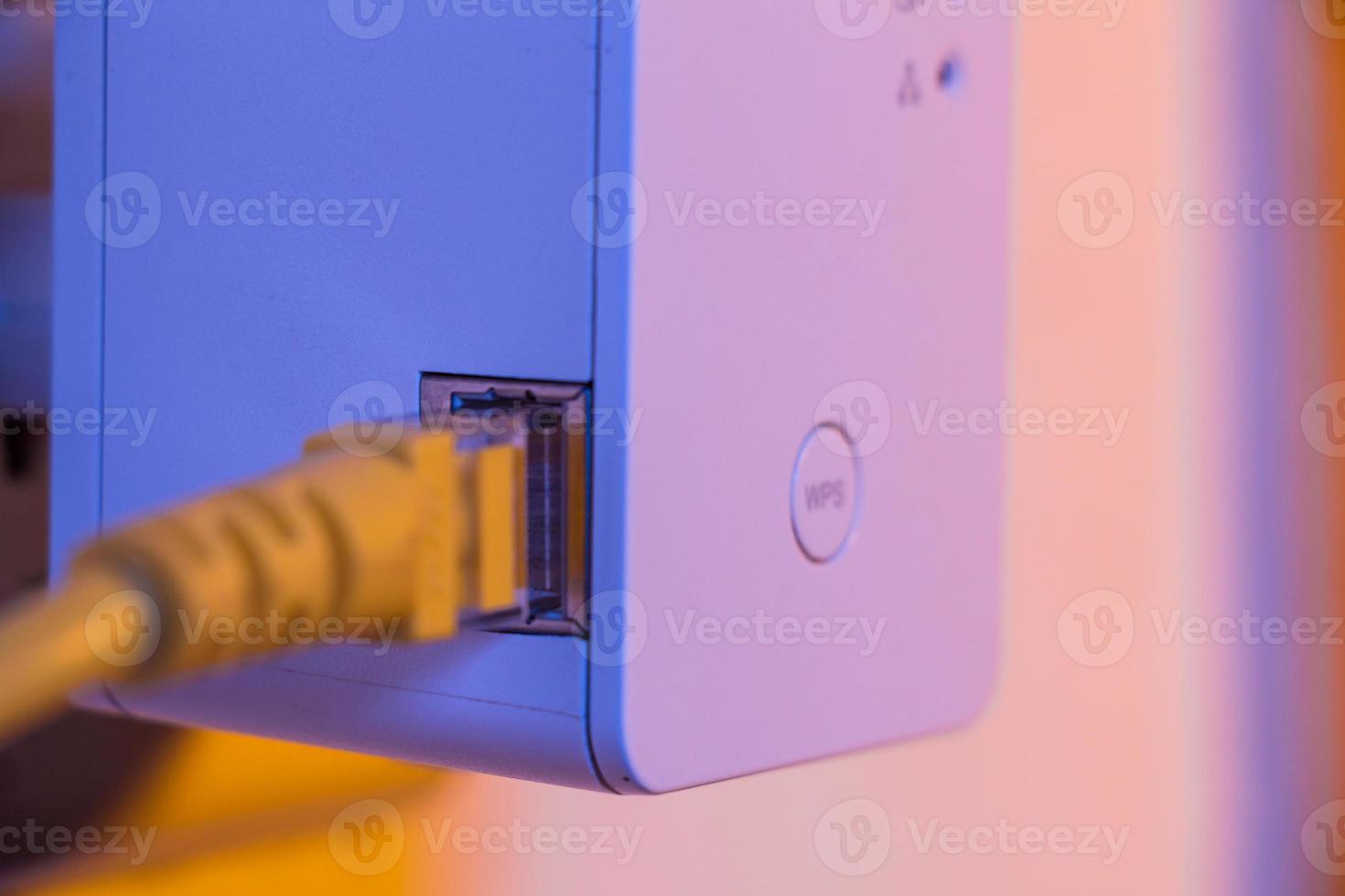 WiFi extender in electrical socket on the wall with ethernet cable plugged in photo