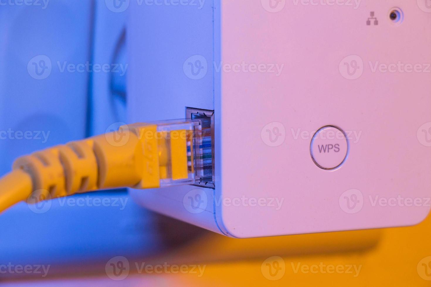 WiFi extender in electrical socket on the wall with ethernet cable plugged in photo