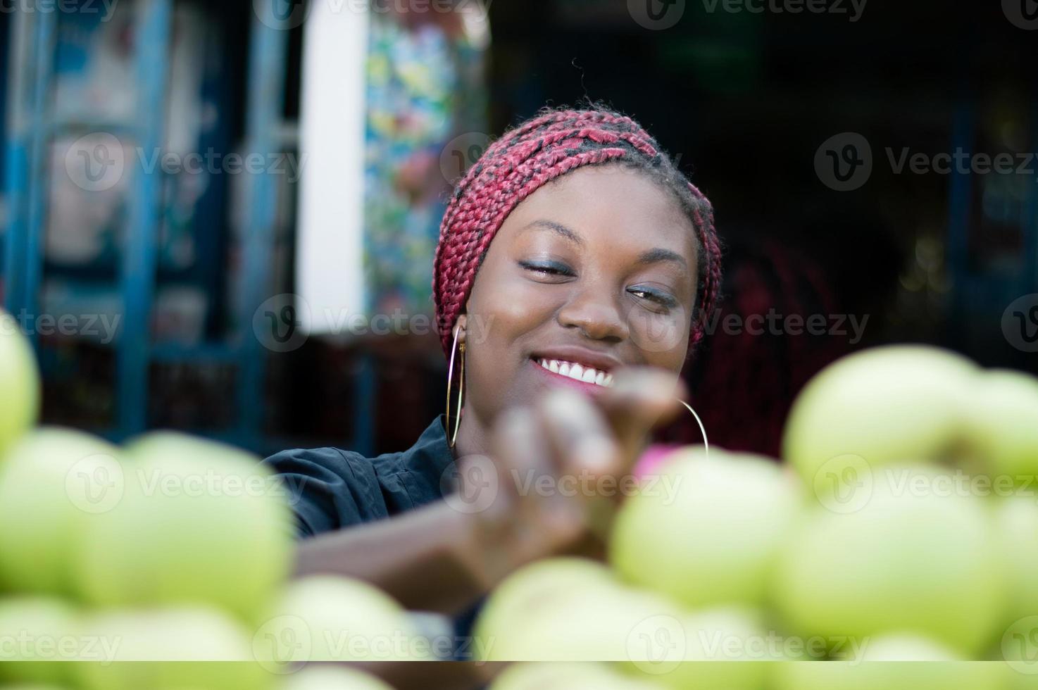 mujer joven sonriente que elige la manzana en el mercado de la calle. foto