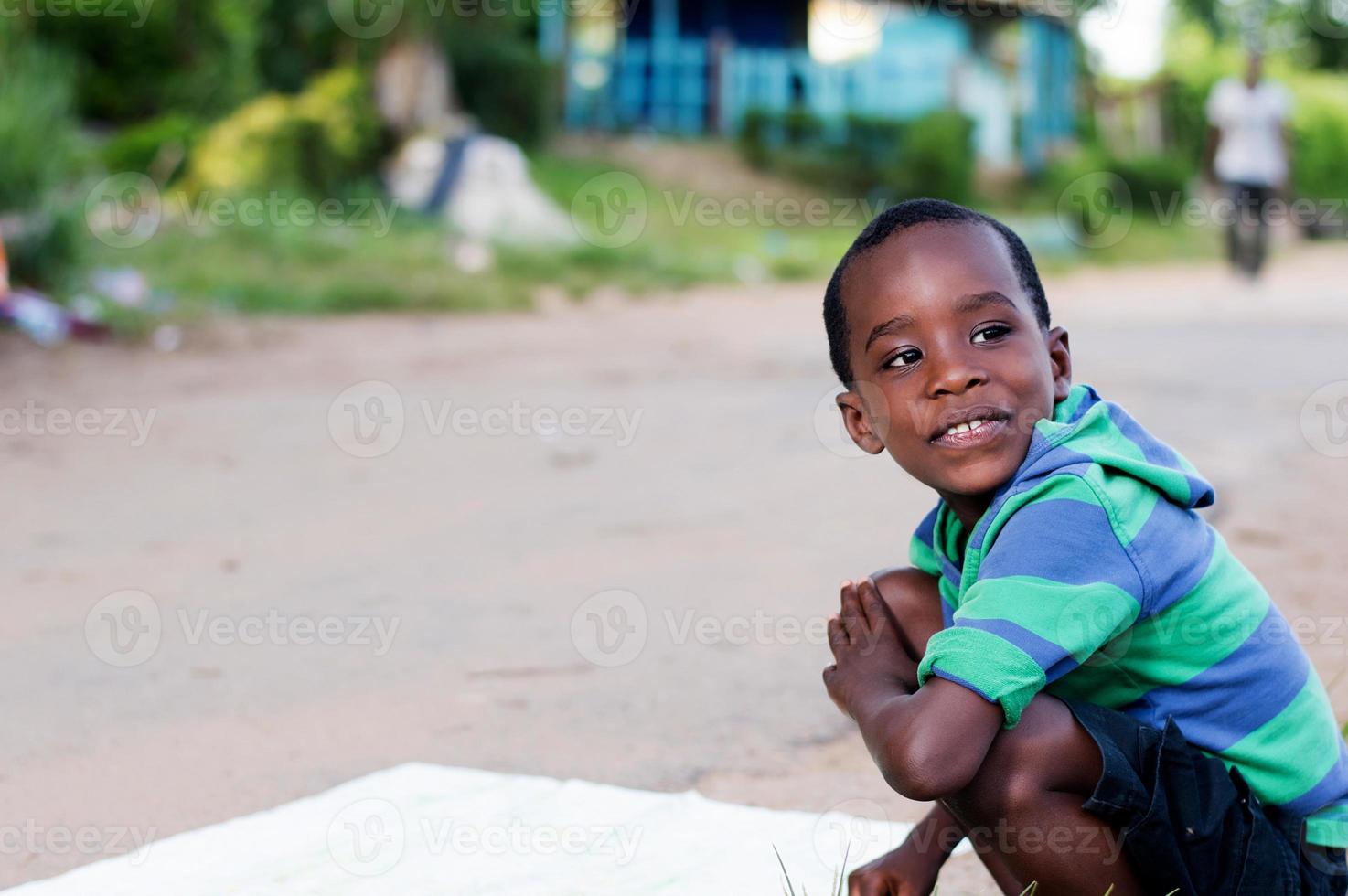 niño alegre agachado al borde de la carretera. foto