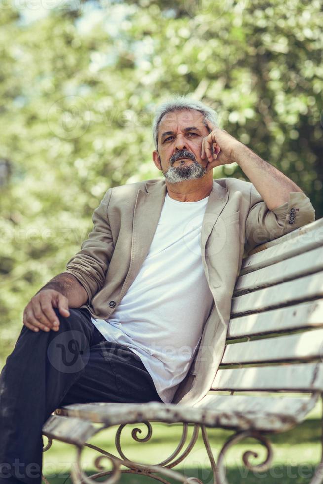 pensativo hombre maduro sentado en un banco en un parque urbano. foto