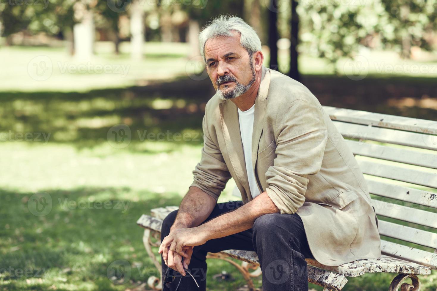 Pensive mature man sitting on bench in an urban park. photo