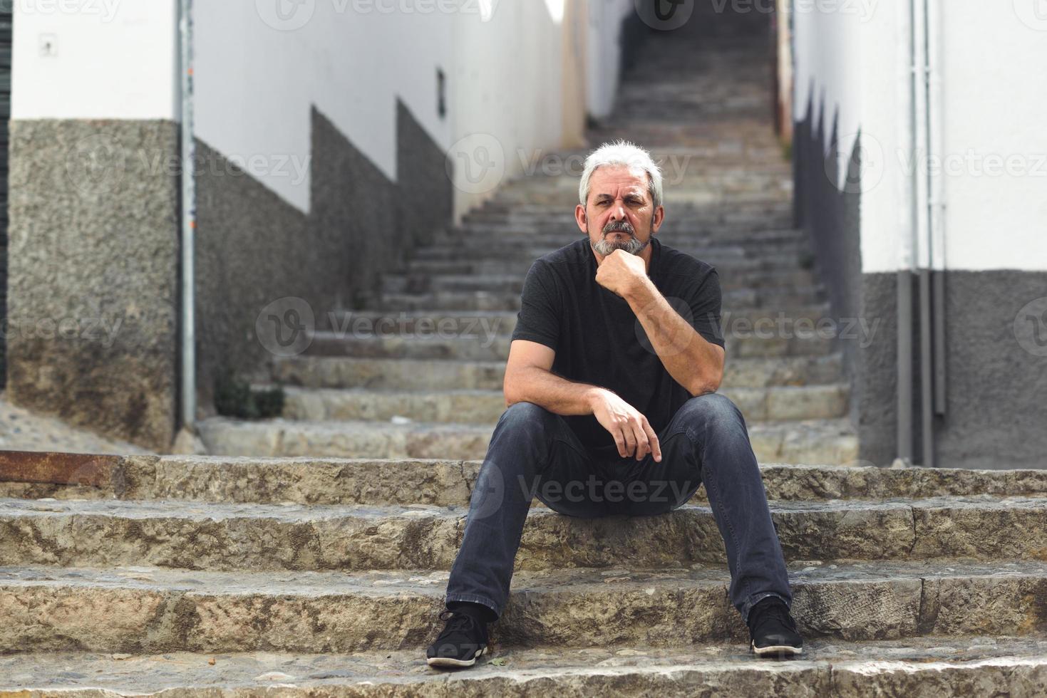 Mature man with white hair sitting on urban steps photo