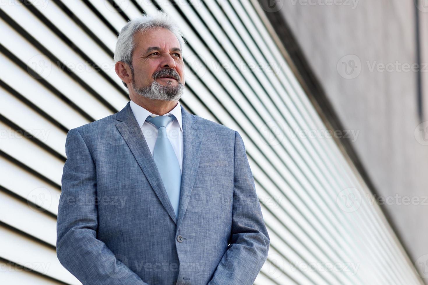 hombre de negocios senior con los brazos cruzados fuera del moderno edificio de oficinas. foto