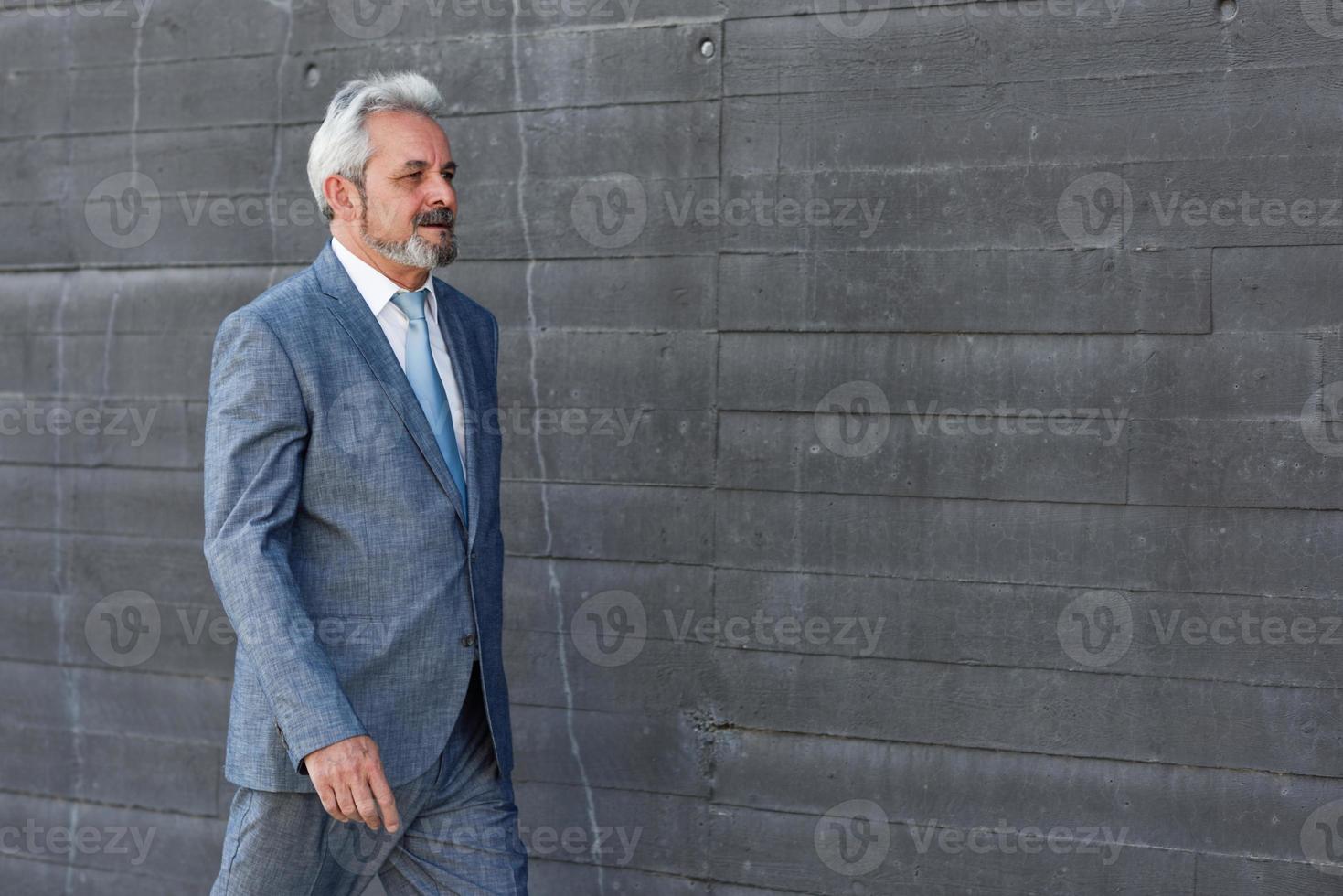 Serious senior businessman walking outside of modern office building. photo