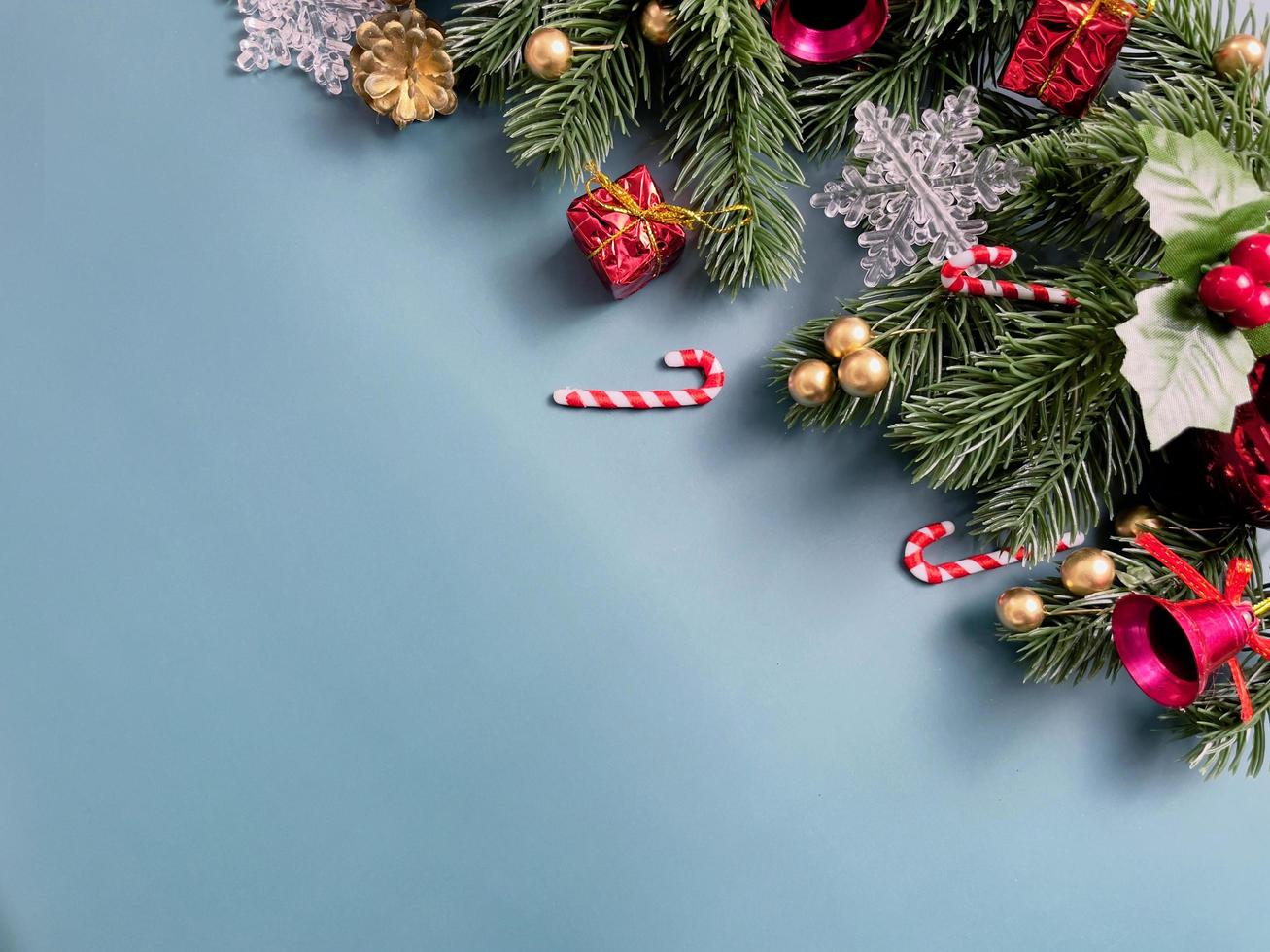 adornos navideños, hojas de pino, bolas doradas, copos de nieve, frutos rojos y frutos dorados sobre fondo azul foto