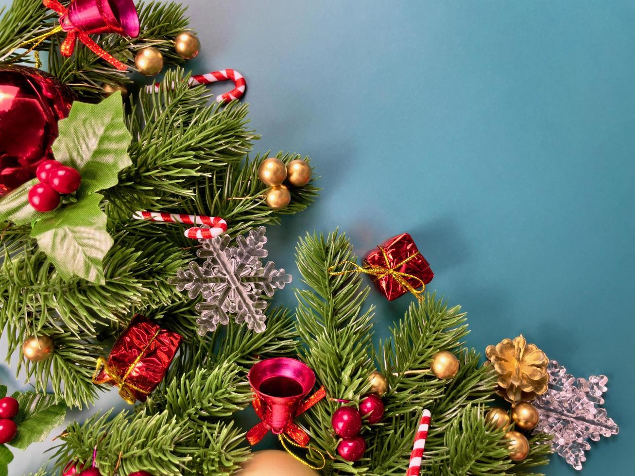 adornos navideños, hojas de pino, bolas doradas, copos de nieve, frutos rojos y frutos dorados sobre fondo azul foto