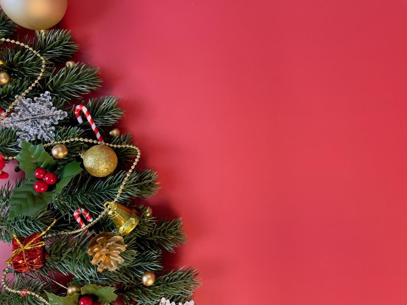 adornos navideños, hojas de pino, bolas doradas, copos de nieve, bayas doradas y frutos rojos sobre fondo rojo foto