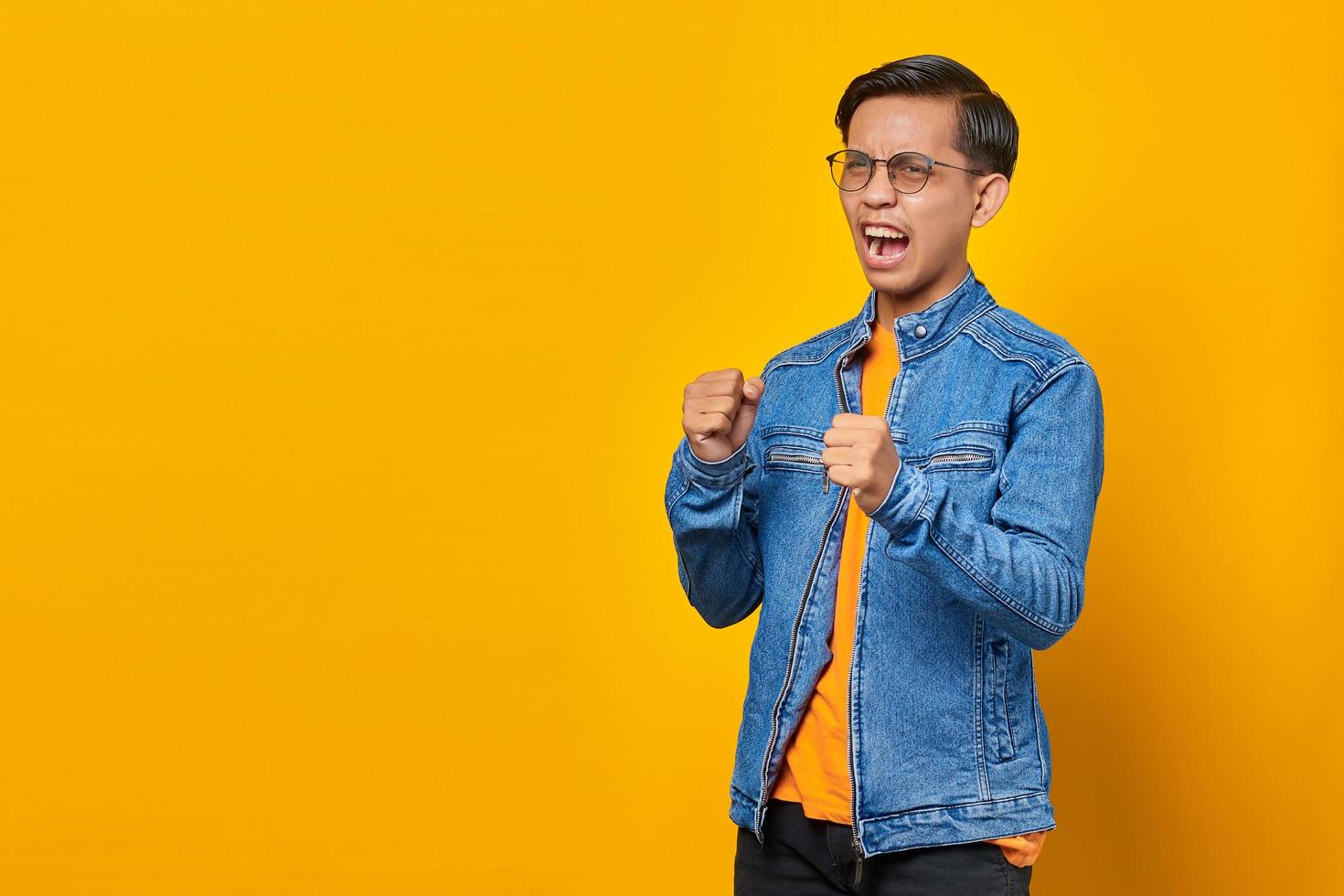 Retrato de hombre asiático joven enojado que muestra el gesto del boxeador sobre fondo amarillo foto