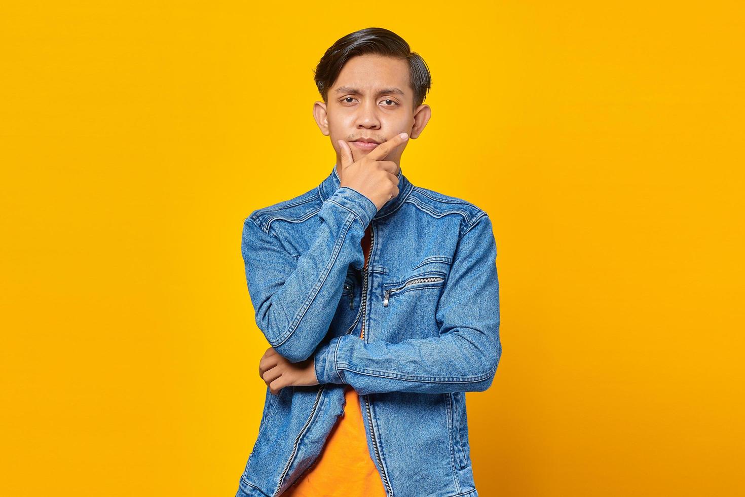 portrait of attractive young asian man holding chin with raised hand and looking at camera photo