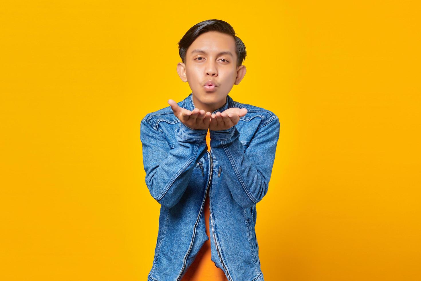 Portrait of charming young Asian man holding palms sending air kiss to girlfriend photo