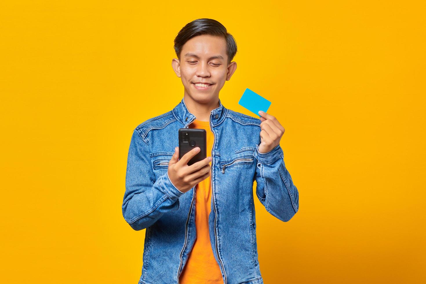 Retrato del hombre asiático sonriente con tarjeta de crédito para pagar con teléfono móvil foto