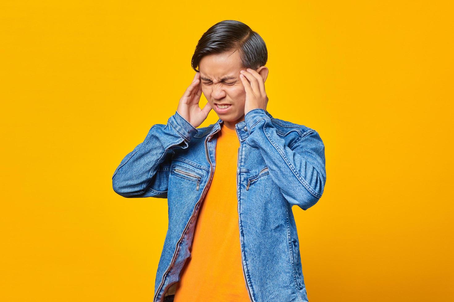 Joven asiático siente dolor de cabeza sobre fondo amarillo foto