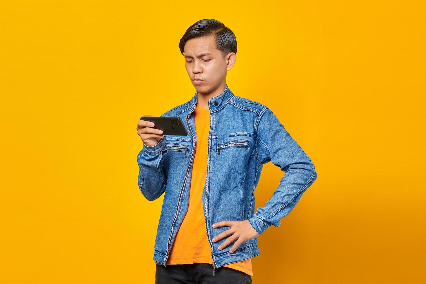 asian man using mobile phone playing game with angry face over yellow background photo