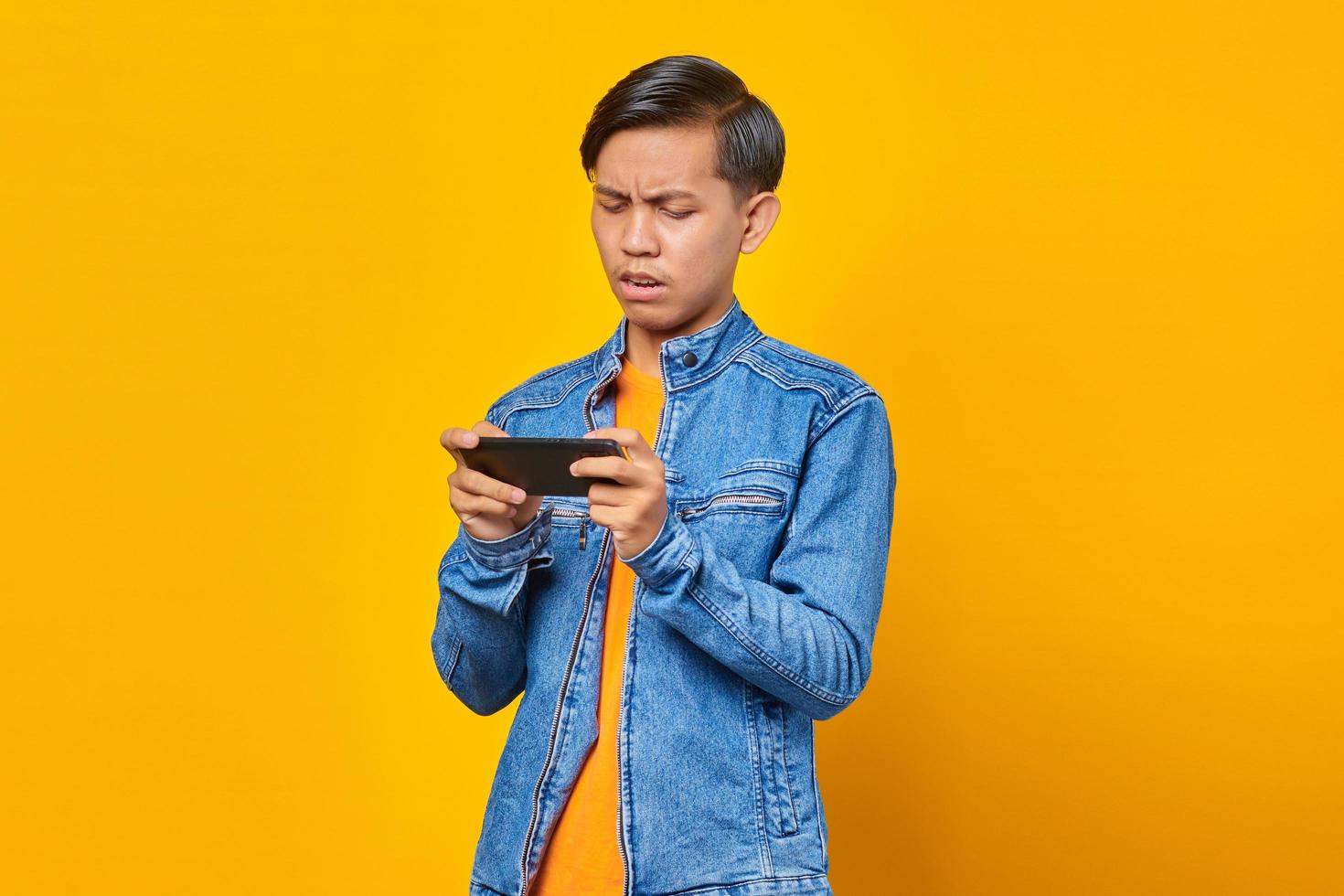 asian man using mobile phone playing game with angry face over yellow background photo