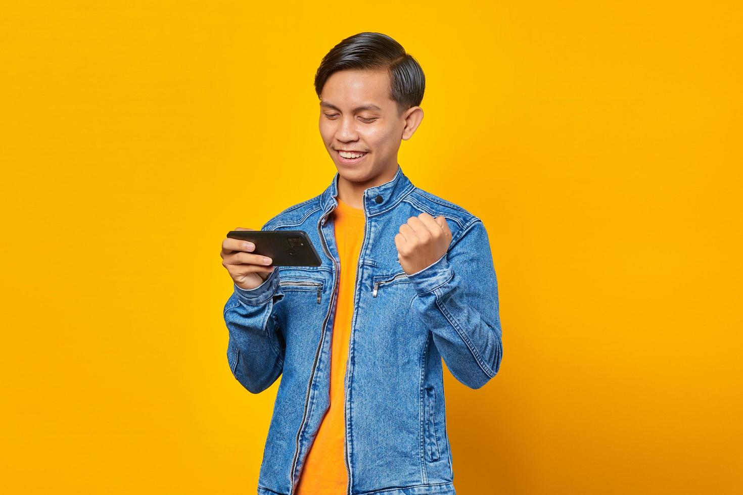 Retrato de hombre asiático entusiasta jugando en el teléfono móvil y celebrando la victoria foto