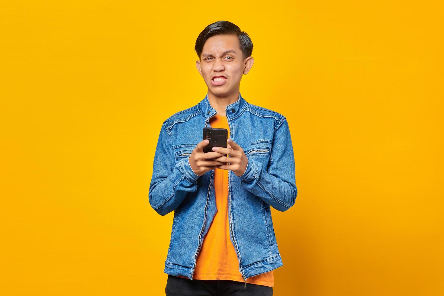 portrait of angry young man looking at camera and holding smartphone photo