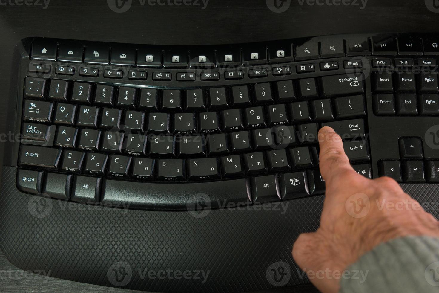 Hombre escribiendo en un teclado con letras en hebreo e inglés foto