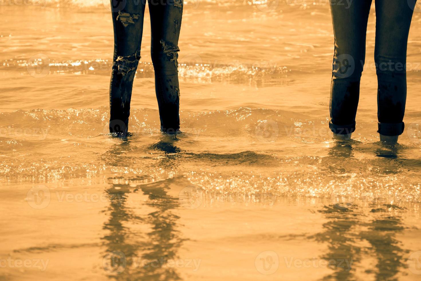 Piernas de mujer en jeans azul de pie en el agua de mar en la costa - tono dorado foto