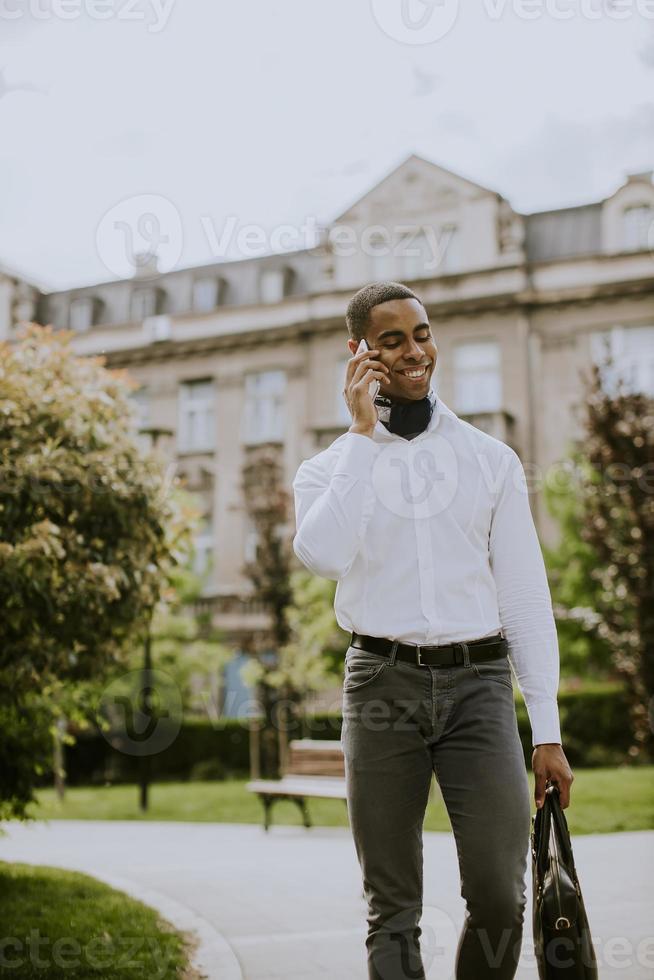 Joven empresario afroamericano mediante un teléfono móvil en una calle foto