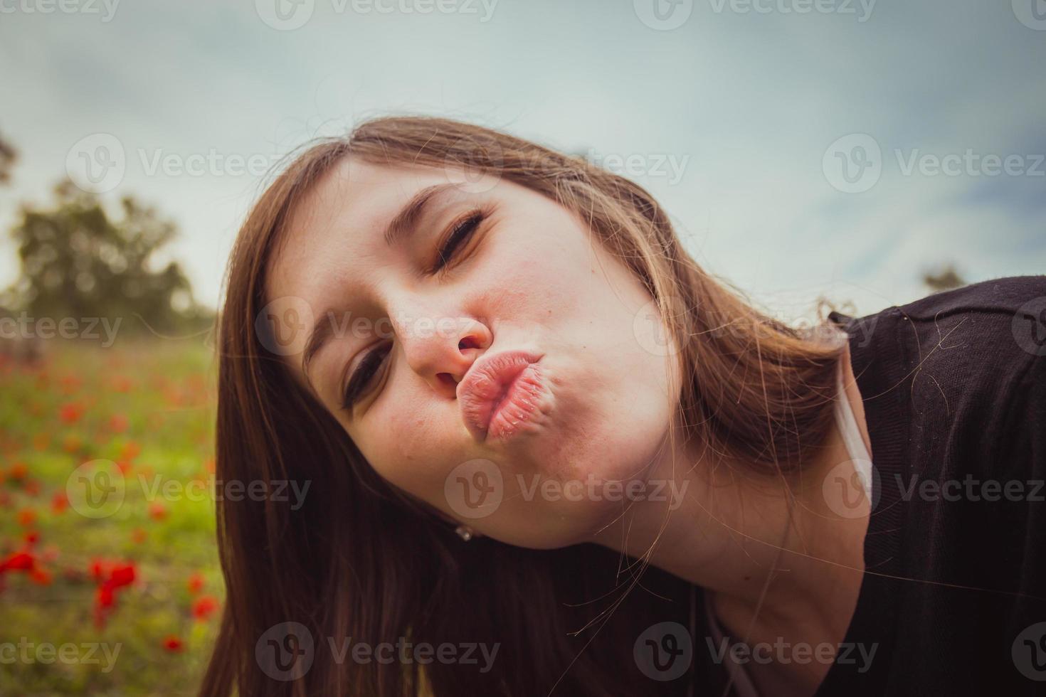 Mujer joven haciendo beso de cara de pato mientras toma una foto selfie con su teléfono inteligente o cámara en el campo de amapolas rojas