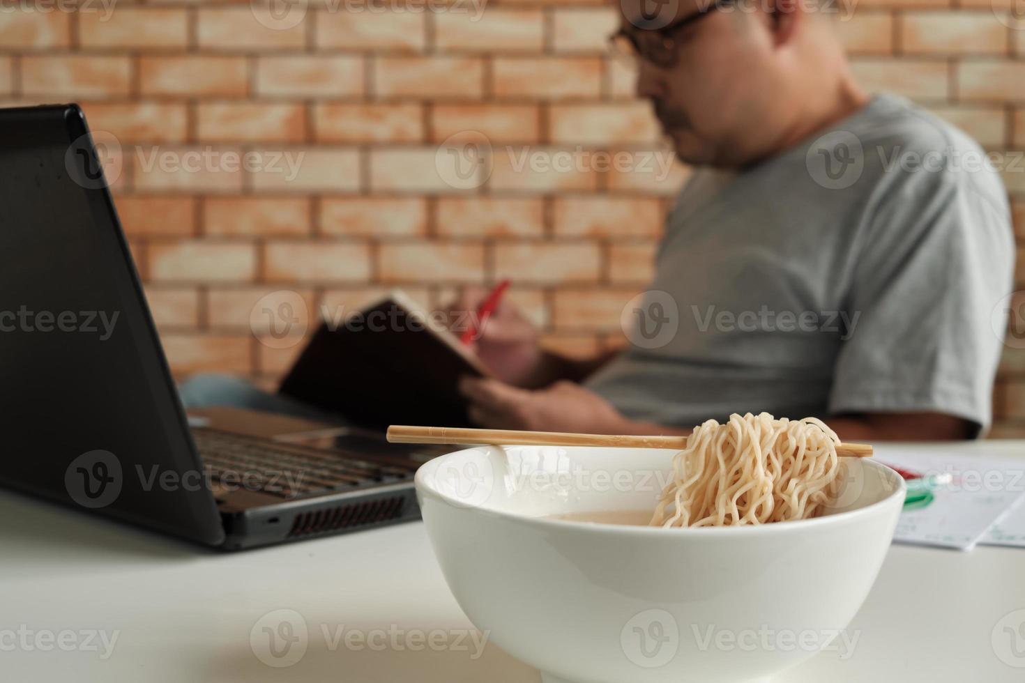 Trabajador tailandés ocupado trabajando con una computadora portátil, use palillos para comer apresuradamente fideos instantáneos durante el almuerzo de la oficina, porque es rápido, sabroso y barato. con el tiempo comida rápida asiática, estilo de vida poco saludable. foto