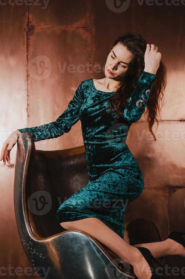 mujer bonita en vestido de terciopelo, sentada en una silla de cuero. concepto de lujo foto