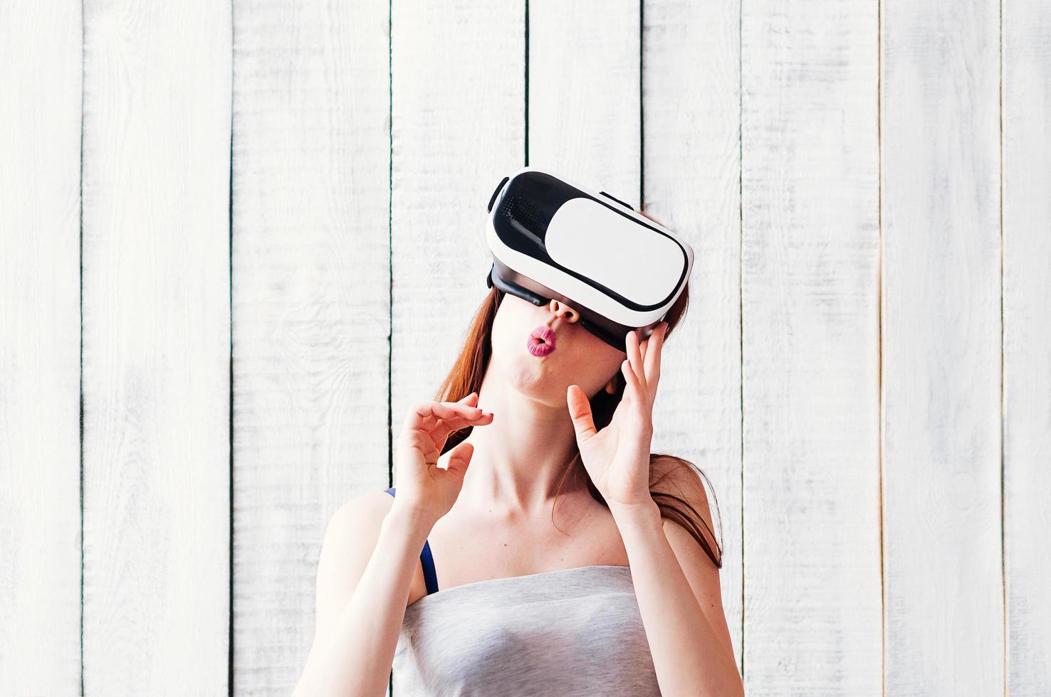 young woman wearing VR glasses, holding her hands at face, white wooden background photo