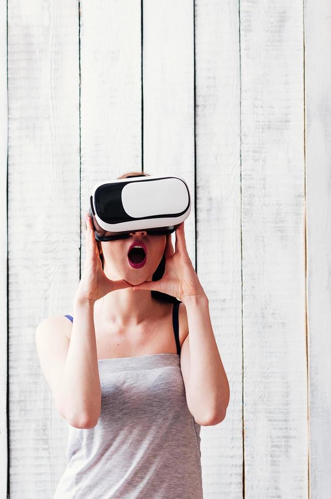 girl wearing VR glasses, excited, holding her hands at face, white wooden background photo