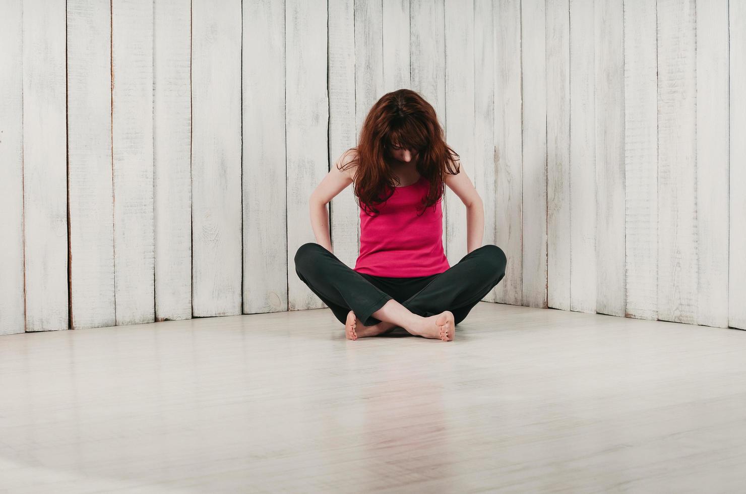 girl in pink sport top, sitting cross-legged on the floor, light background photo