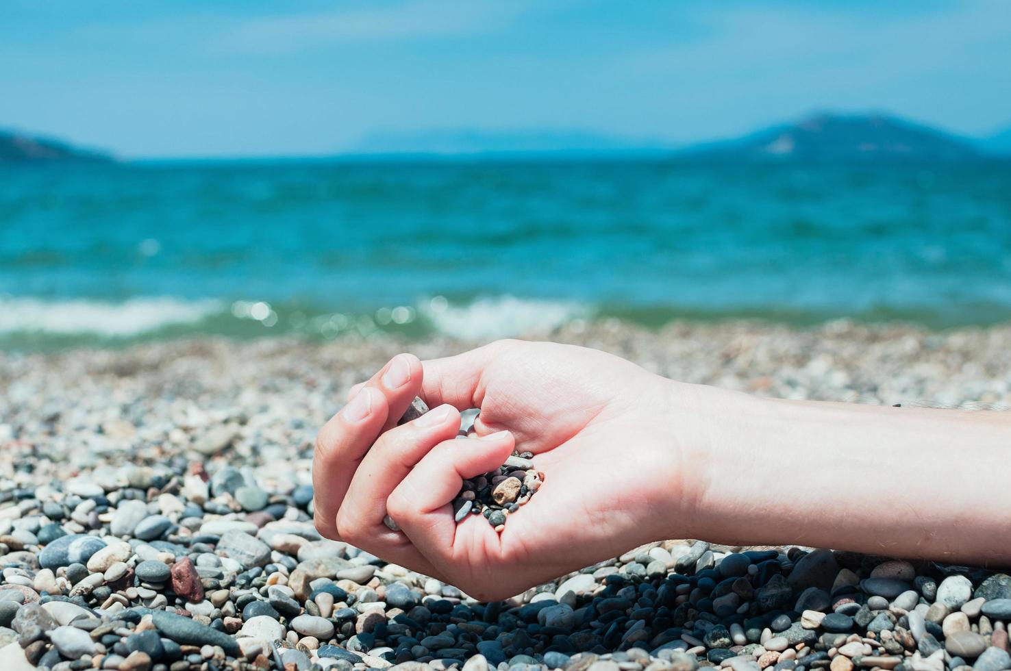 Hand holding pebbles on beach, turquoise sea water in background photo