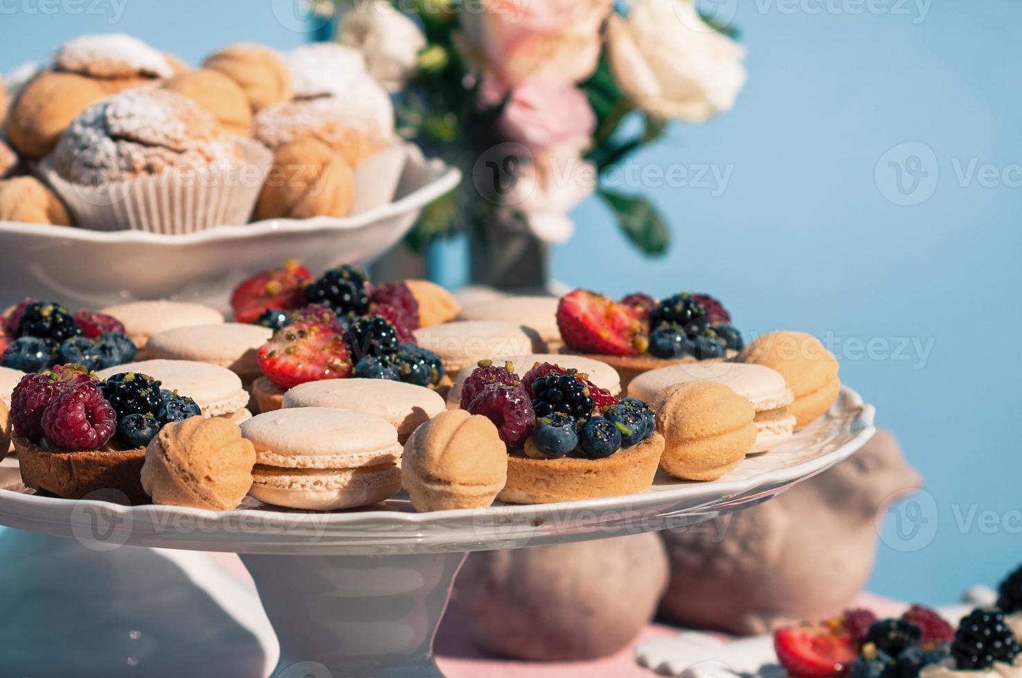 delicioso buffet dulce con magdalenas, macarrones, otros postres, fondo azul foto