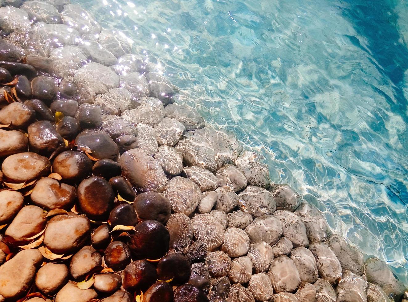 Big pebbles and stones under blue transparent water on the beach photo