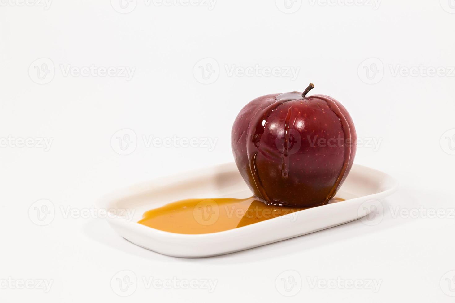 Manzana roja con gotas de miel en un plato blanco con miel aislado sobre un fondo blanco. foto