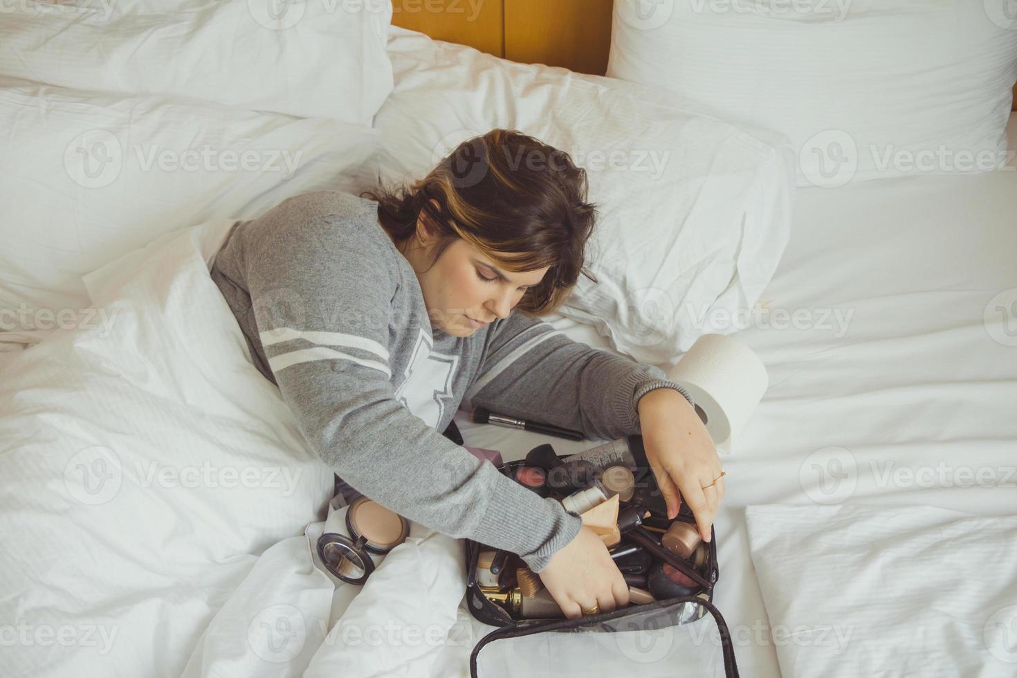 Mujer aplicando maquillaje mientras está acostada en su cama foto