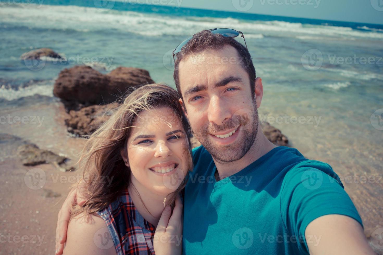 Young couple taking selfie with smartphone or camera at the beach photo