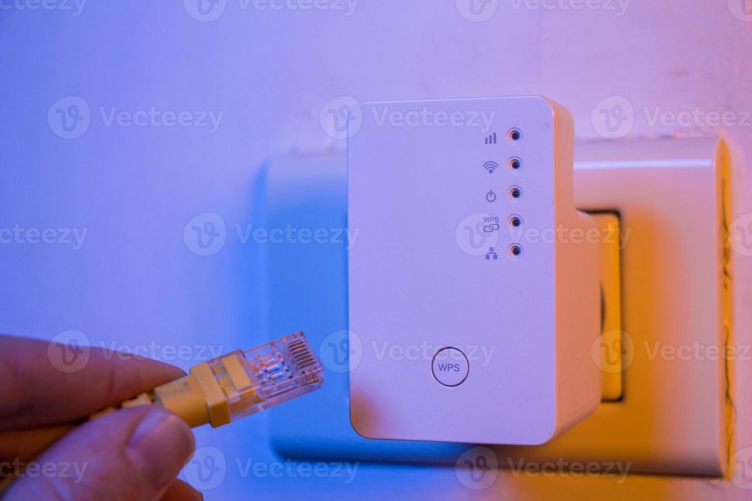 Man insert ethernet cable into WiFi extender device which is in electrical socket on the wall photo