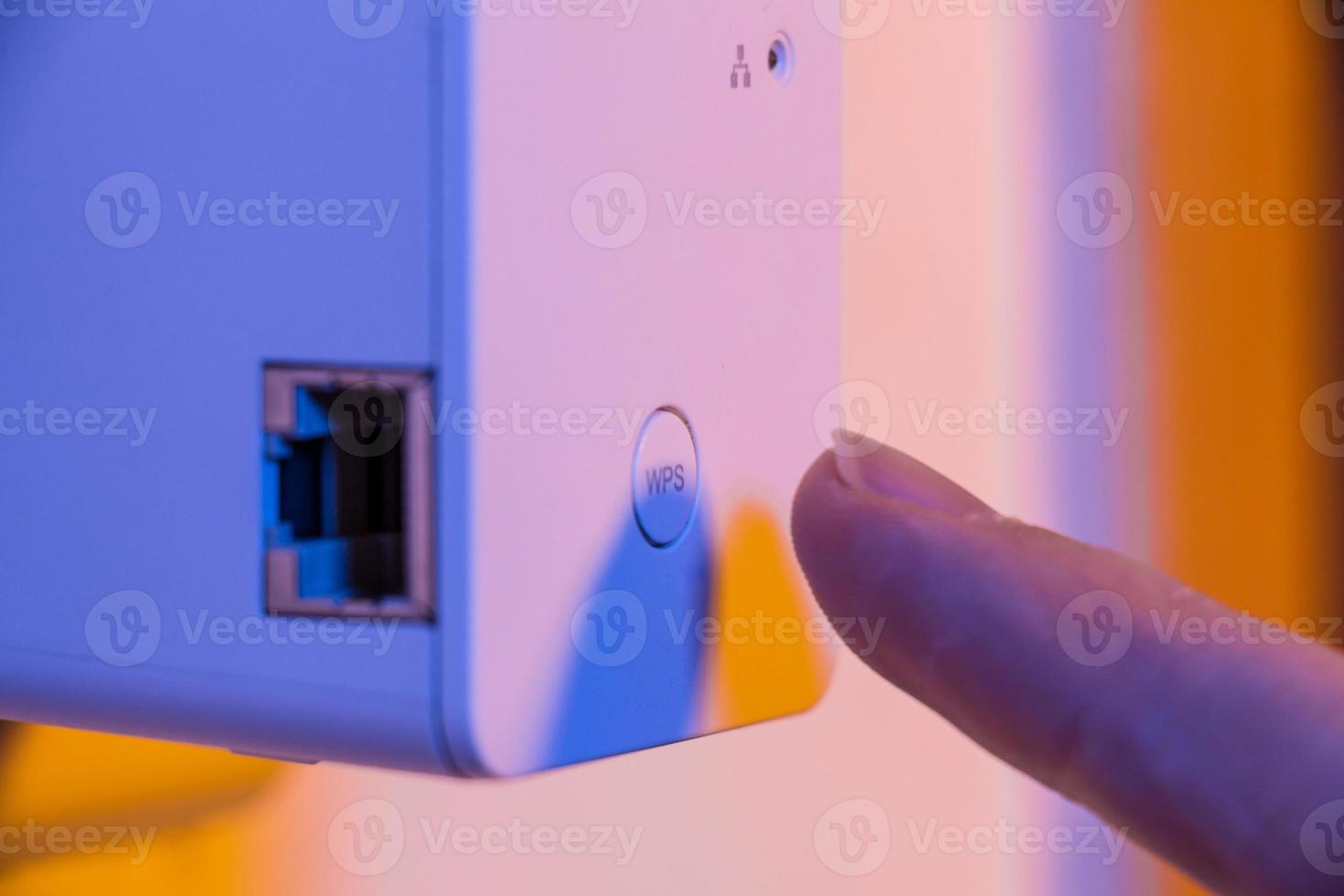 Man press with his finger on WPS button on WiFi repeater which is in electrical socket on the wall photo