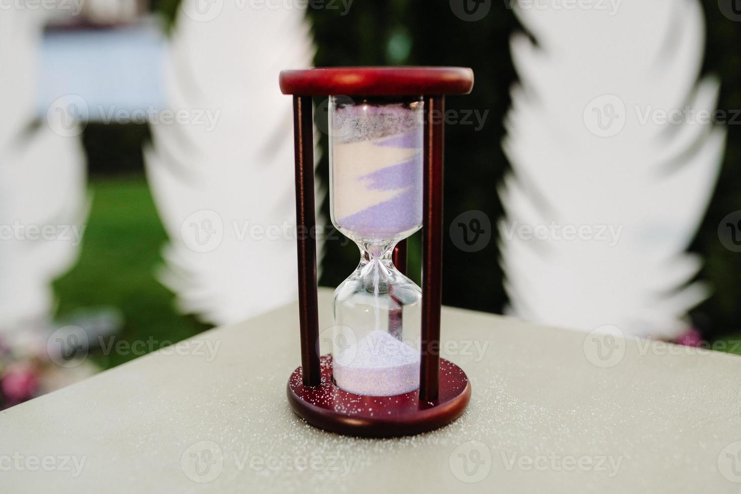 white sand hourglass in brown wood on table photo