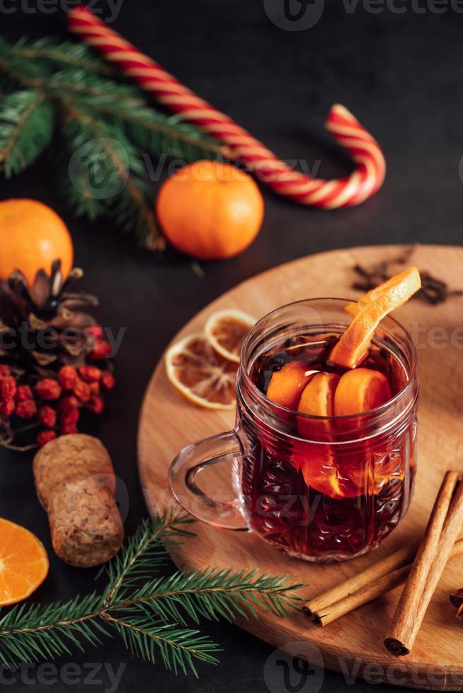 Hot mulled wine in glass cup on dark background. Warm Christmas drink with spices and fruits. photo